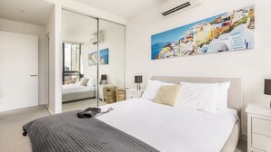 Un dormitorio moderno con una cama grande, una mesita de noche, un espejo y aire acondicionado instalado en la pared.