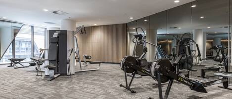 A modern gym with various exercise equipment, large windows, and a carpeted floor.
