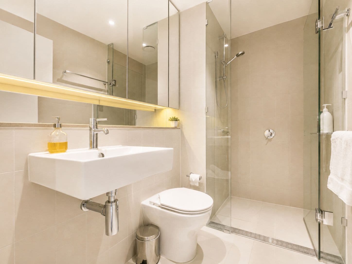 Un baño moderno con cabina de ducha de vidrio, un lavamanos blanco y un inodoro.