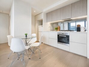 Une cuisine moderne avec des meubles blancs, un four en acier inoxydable et une table à manger en verre, assortie de chaises blanches.