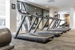 Une rangée de tapis de course dans la salle de sport d’un hôtel, avec un panneau indiquant « Wi-Fi gratuit » sur le mur.