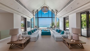A spacious living area with a large window offering a view of the sea. There are multiple seating arrangements, including sofas and a coffee table. - Villa Vikasa (Pa Klok)