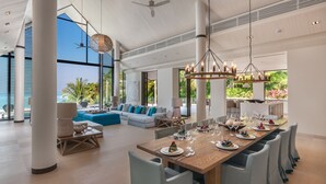 A spacious living area with a large dining table set for a meal, a cozy seating area with a sofa, and large windows offering a view of the outdoors. - Villa Vikasa (Pa Klok)