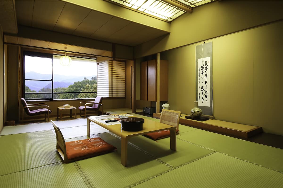 A traditional Japanese room with tatami flooring, a low table, and a view of mountains through the window.