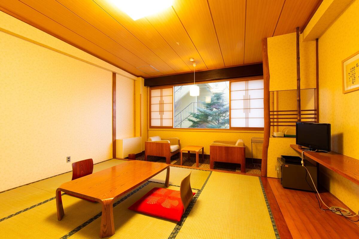 A traditional Japanese-style room with tatami flooring, a low wooden table, and a television on a wooden stand.