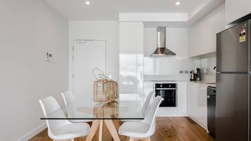 Una cocina moderna con una mesa de comedor de vidrio, sillas blancas, un refrigerador de acero inoxidable y un horno empotrado.