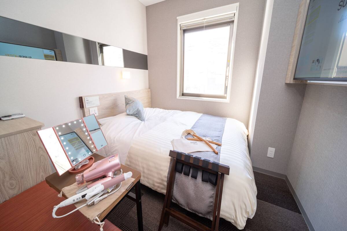A hotel room with a bed, a vanity with a mirror, a hairdryer, and a suitcase.