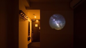 A hotel room with a bed, a nightstand, a mirror, a door, and a wall-mounted projector displaying the Milky Way. - Super Hotel Kumamoto Yatsushiro (Yatsushiro)