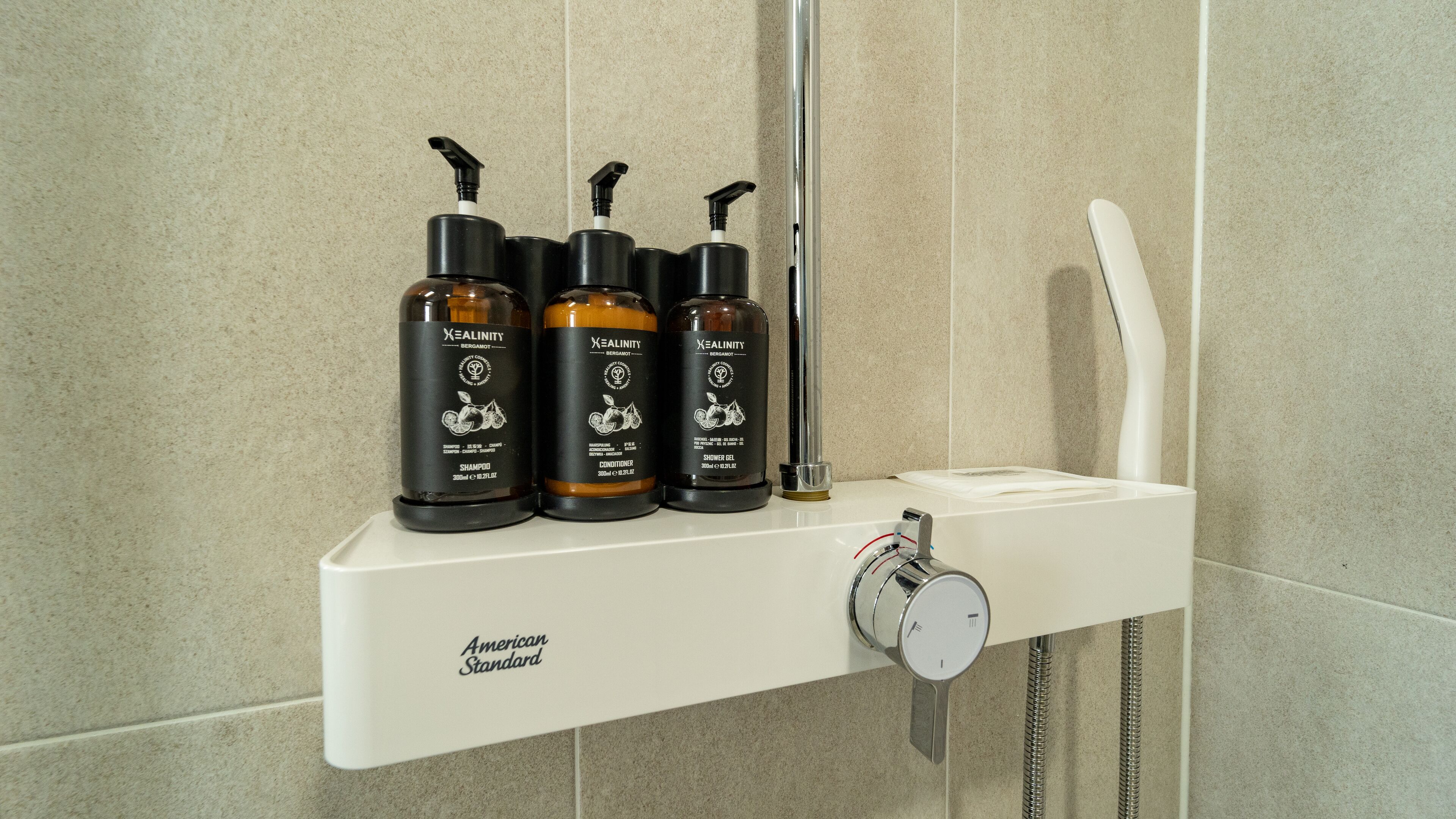 A bathroom shelf with three bottles of shampoo, conditioner, and shower gel, a handheld showerhead, and a faucet.
