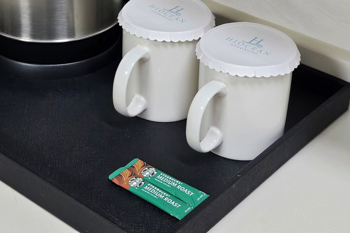 Deux tasses en céramique blanche, dotées de couvercles, posées sur un plateau noir, une bouilloire en acier inoxydable et un paquet de café Starbucks, torréfaction moyenne.
