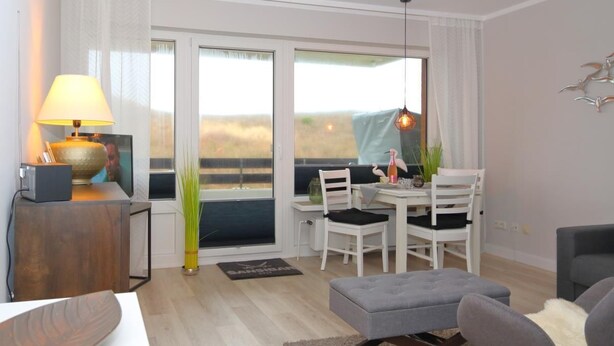 A modern living room with a dining area, large windows, a lamp, and a view of the outdoors. - Apartment Widlak - Beach crossing K.Christiansen (Sylt)