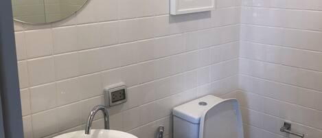 Un baño con un espejo redondo, un lavabo blanco, un inodoro y una obra de arte enmarcada en la pared.