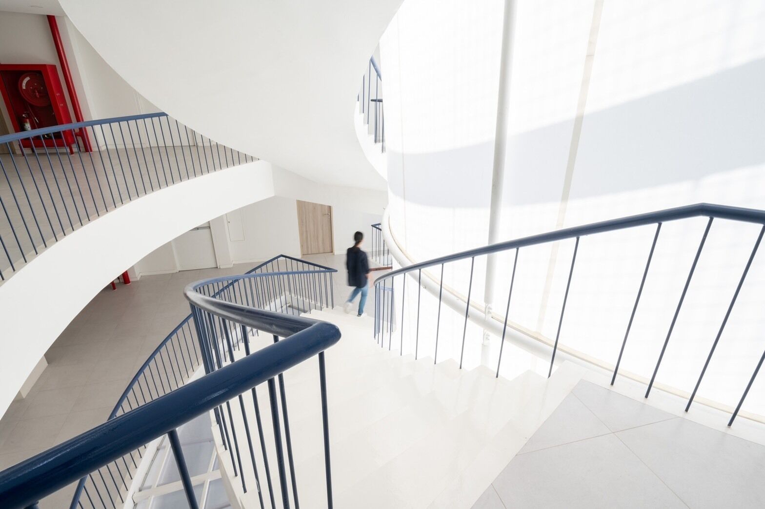 A modern interior with a curved staircase, white walls, and a red fire extinguisher.