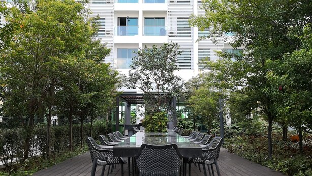 An outdoor dining area with a long table and chairs, surrounded by trees and a building in the background. - Cybersquare by Flexihome (Cyberjaya)