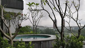 A rooftop pool area with a circular hot tub, surrounded by greenery and overlooking a cityscape. - Cybersquare by Flexihome (Cyberjaya)