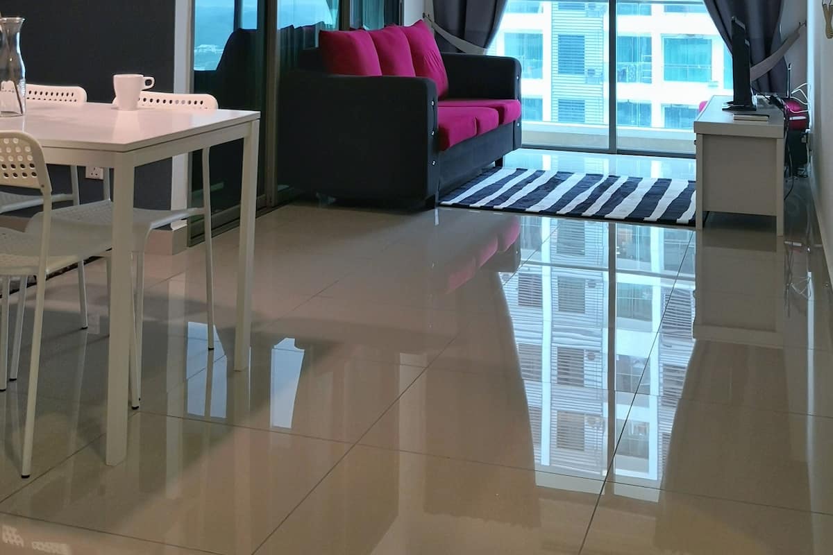 A modern living room with a white table, chairs, a sofa with pink cushions, and a large window offering a city view.