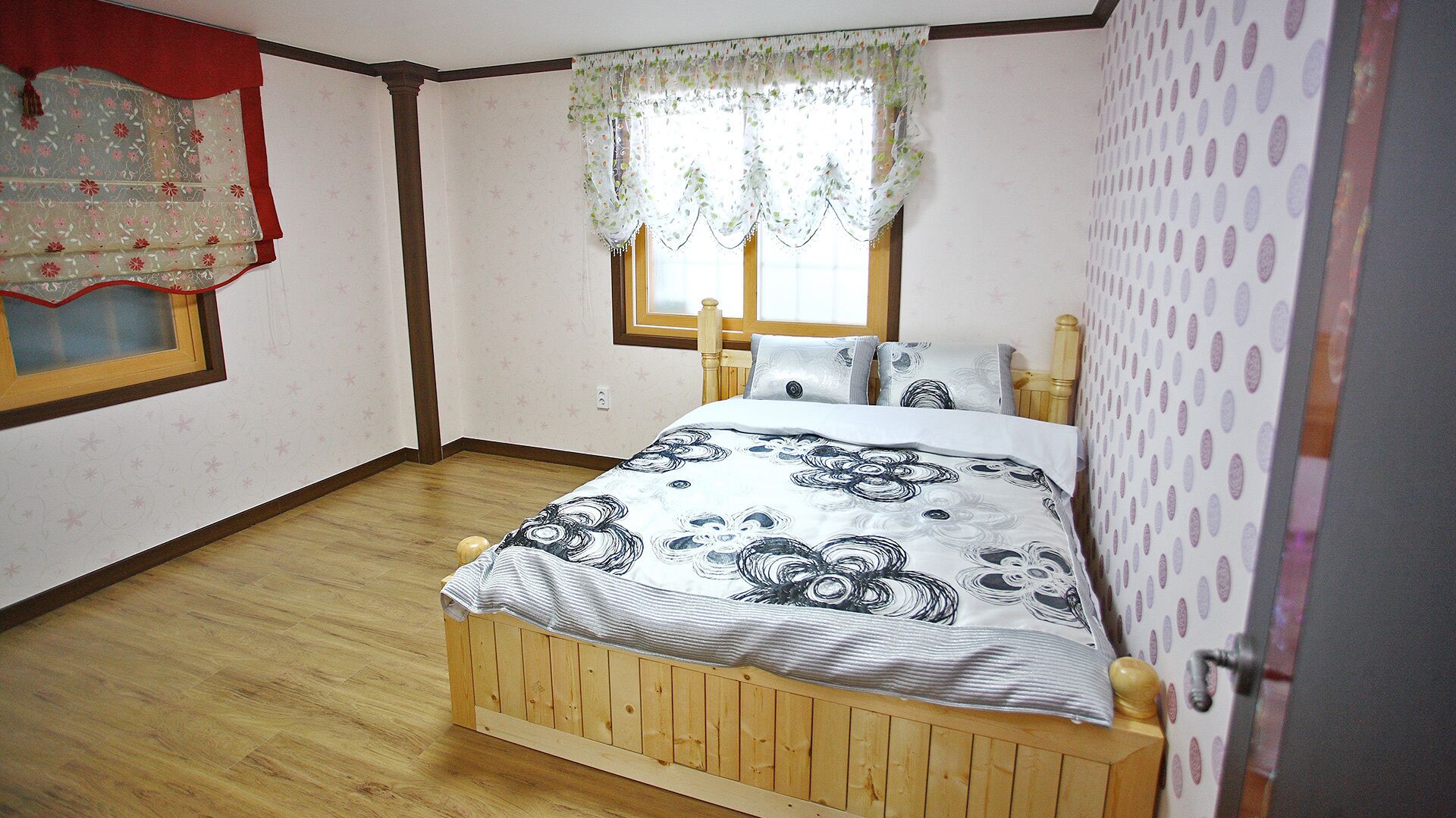 Een slaapkamer met een houten bed, een raam met kantgordijnen en behang met een patroon.