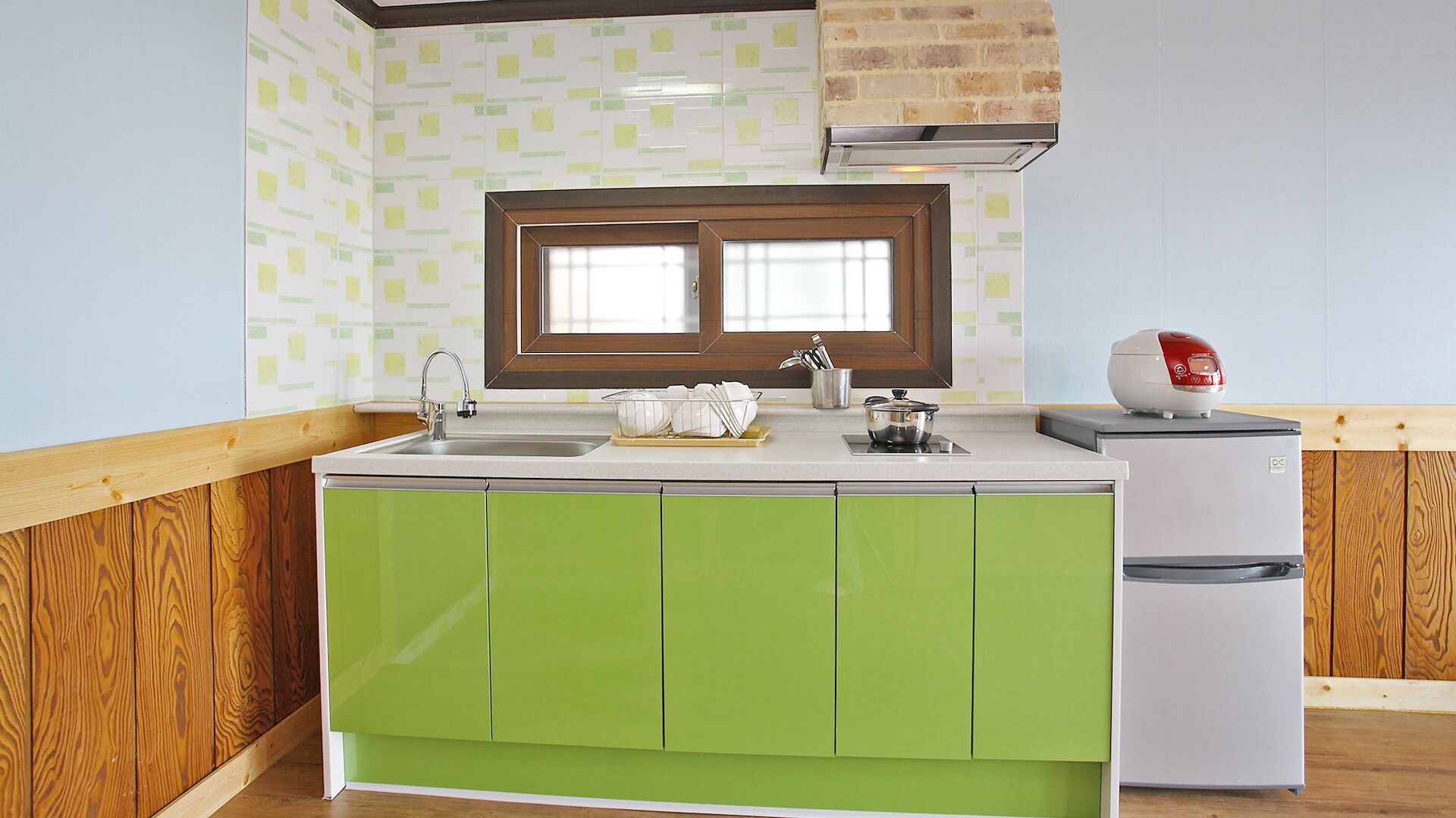 A kitchen with green cabinets, a white countertop, a window with blinds, a stove, and a refrigerator.