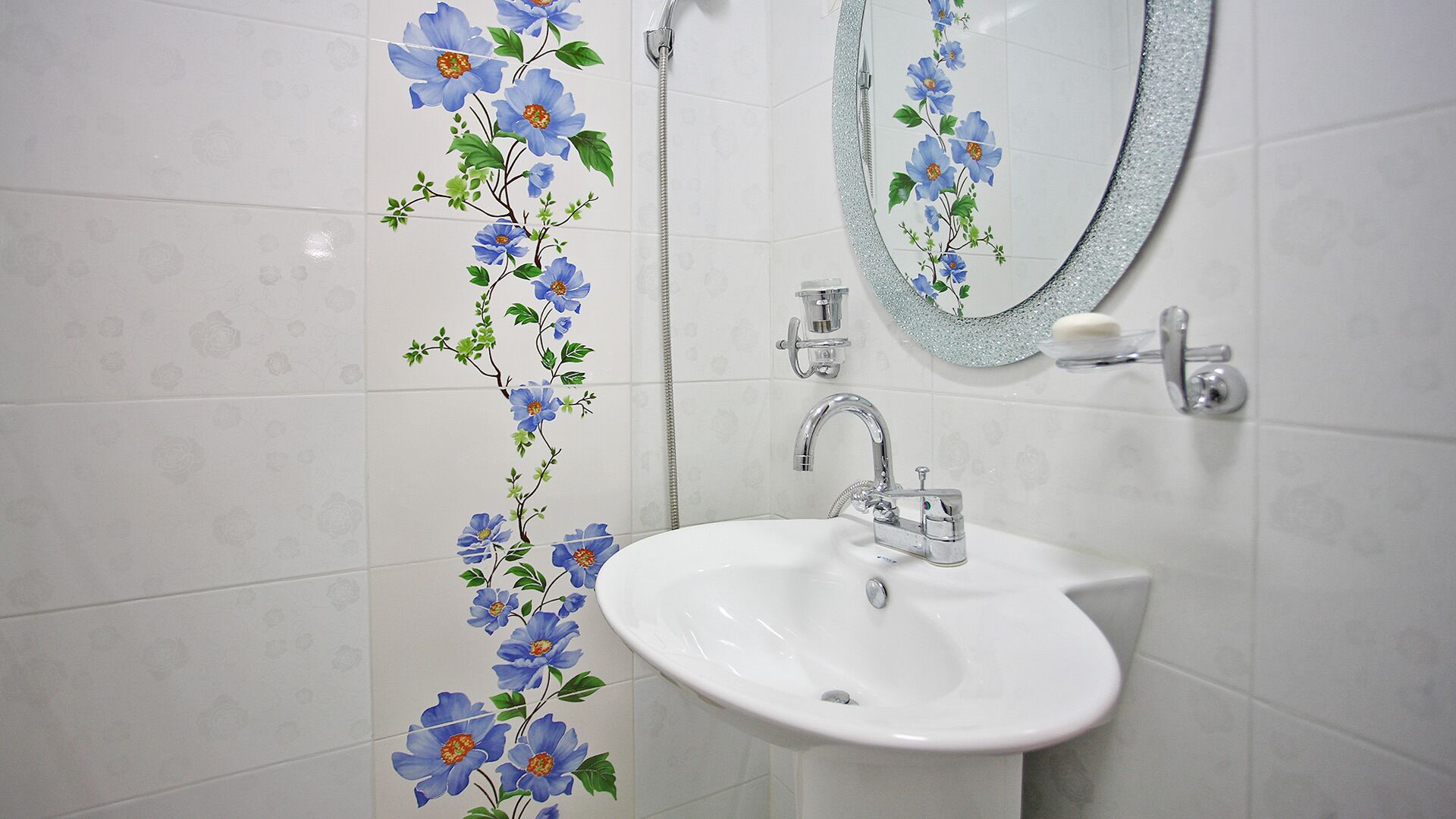 A bathroom with a white sink, a mirror, and floral wall tiles.