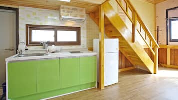 Een keuken met groene kasten, een witte koelkast en een houten trap.