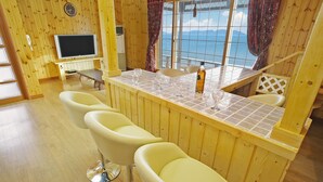 A wooden interior with a bar area, bar stools, a television, and a view of the sea. - Morwenna Pension (Taean)