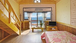 A wooden cabin room with a bed, a TV, a table with a vase, and a view of the sea. - Morwenna Pension (Taean)