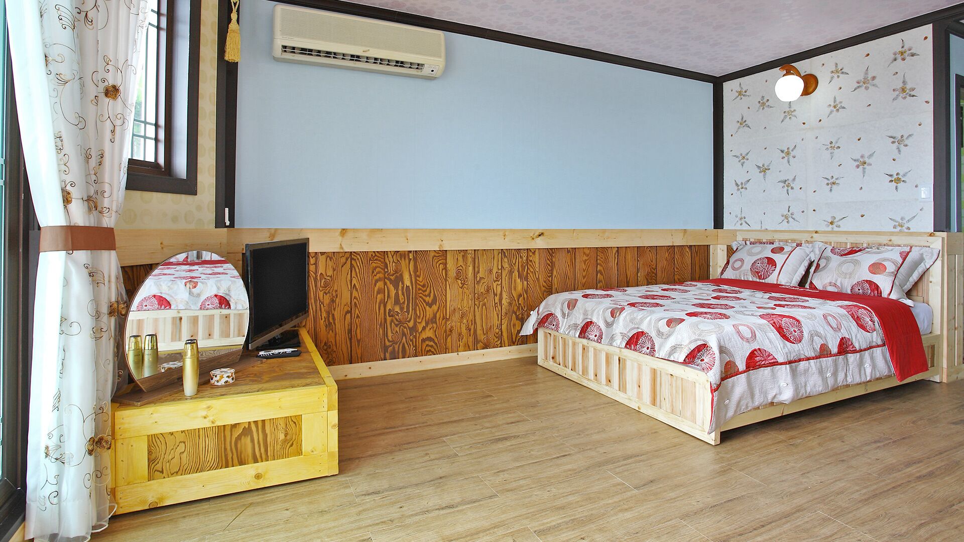 A bedroom with a wooden bed, a wooden nightstand, a TV, and a wall-mounted air conditioner.