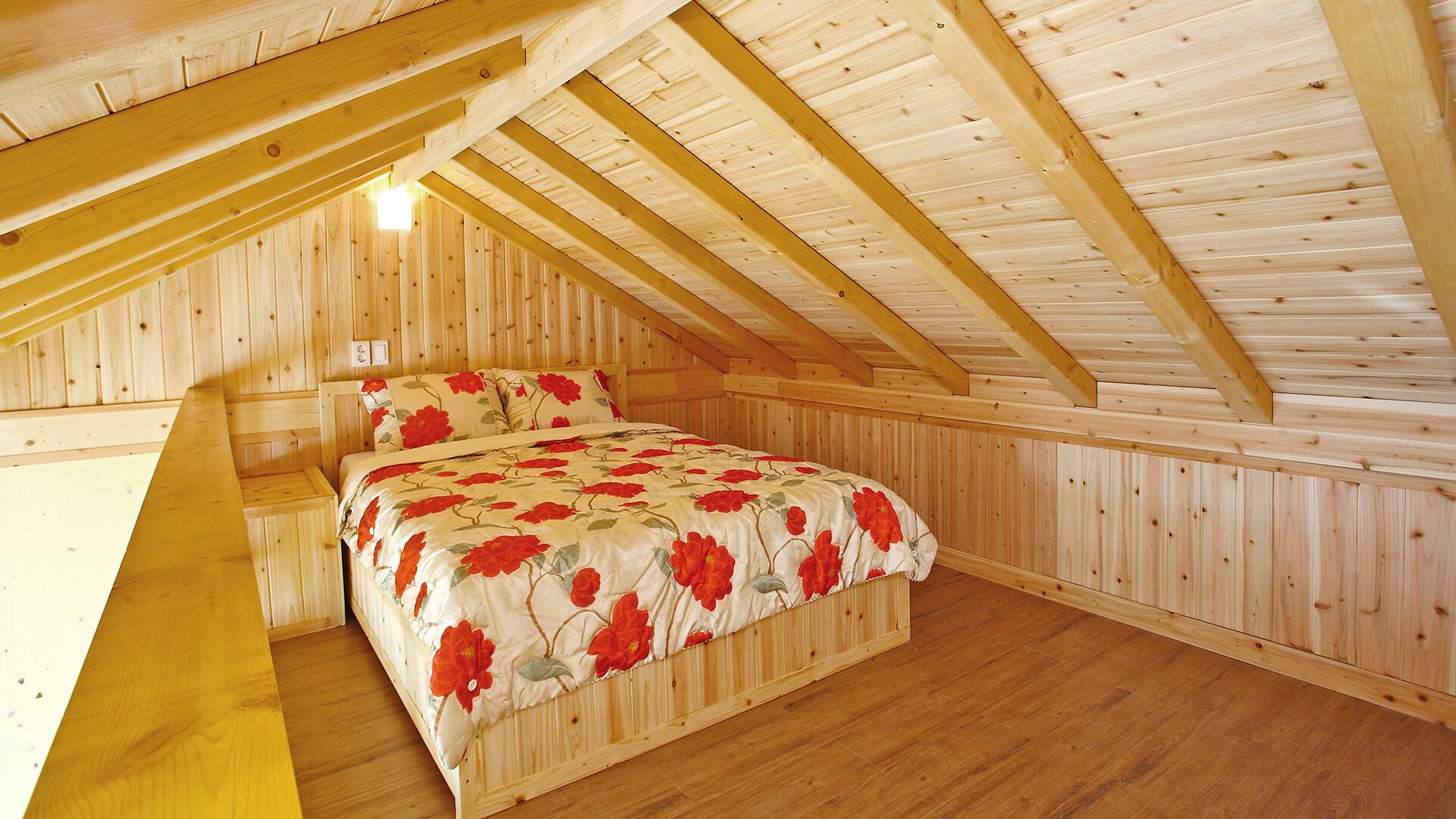 Un dormitorio con techo inclinado de madera, una cama con ropa de cama floral y paredes de madera.