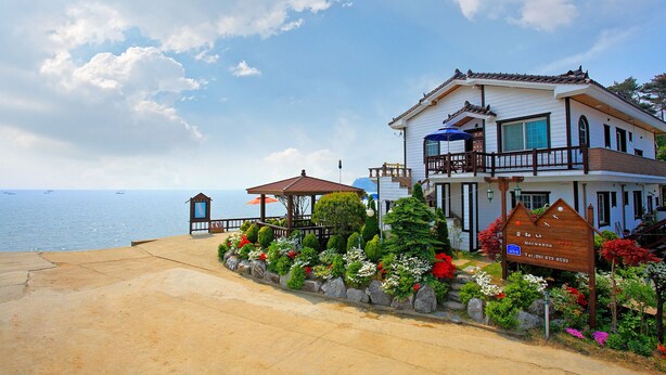 A coastal hotel with a balcony, a garden with flowers, and a view of the sea. - Morwenna Pension (Taean)