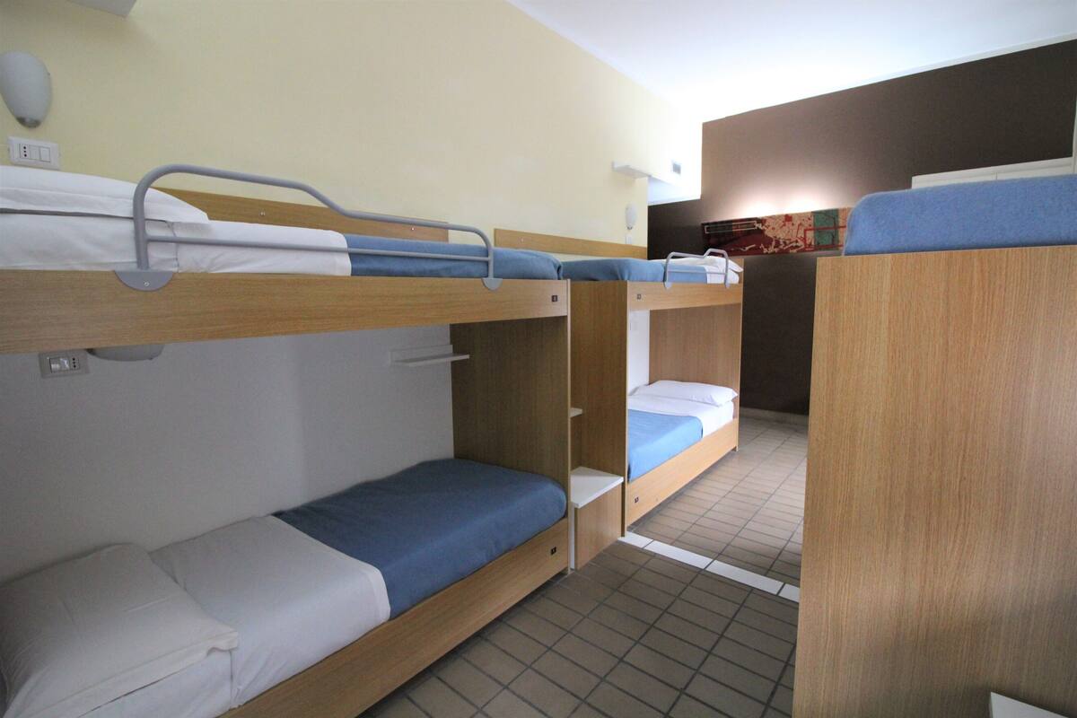 A bunk bed room with wooden bunk beds, white bedding, and a tiled floor.