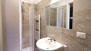 A bathroom with a glass-enclosed shower, a white sink with a mirror above it, and beige tiled walls. - New Generation Hostel Tirana Center (Tirana)