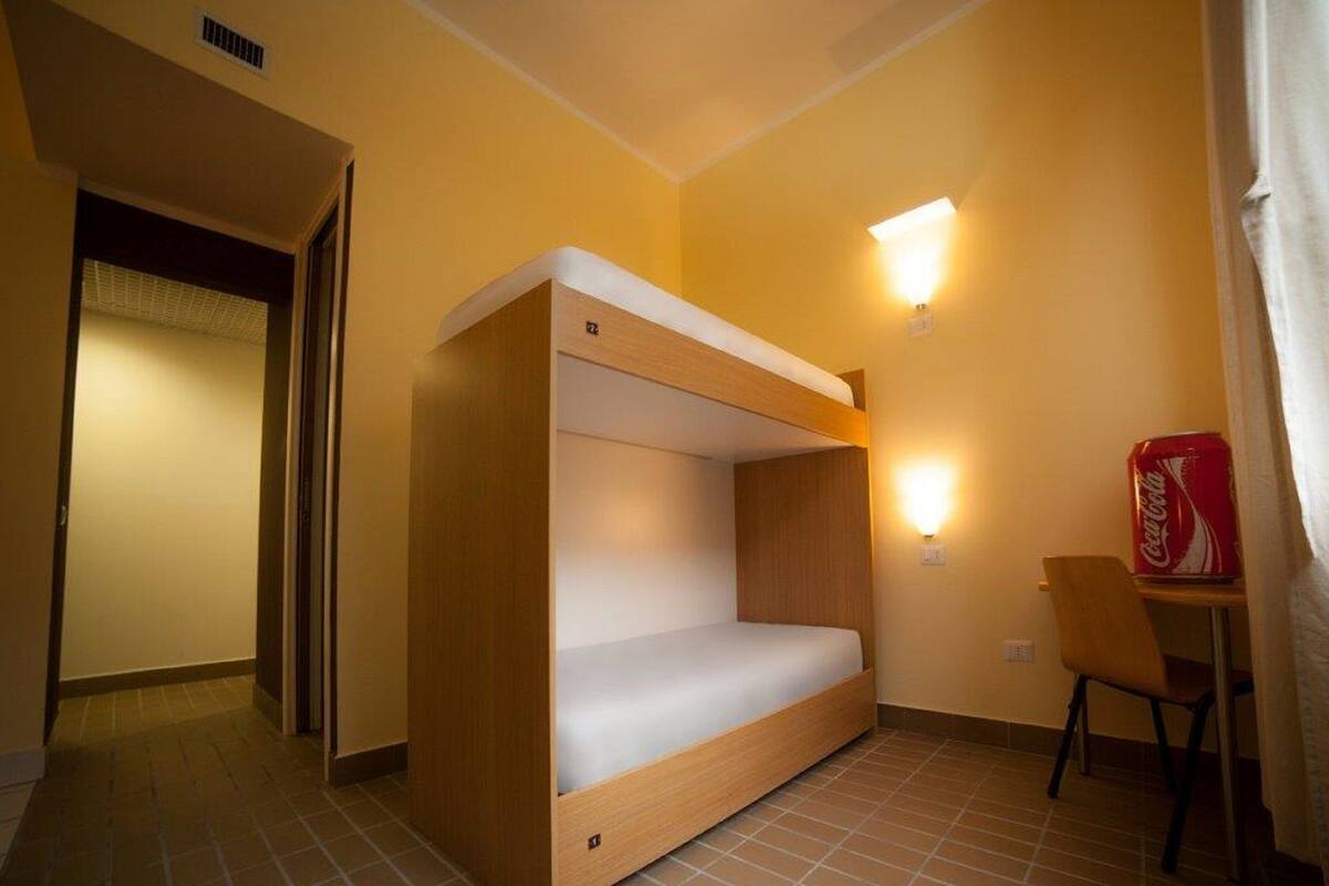 A compact room with a bunk bed, a small table, a chair, and a wall-mounted light fixture.