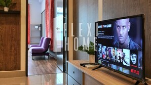 Een moderne woonkamer met een houten tv-meubel, een flatscreen-televisie met een streamingdienst interface, een paarse fauteuil en een glazen deur die naar een andere kamer leidt.