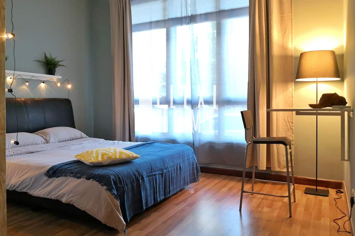 A bedroom with a bed, a chair, a lamp, and a window with curtains.