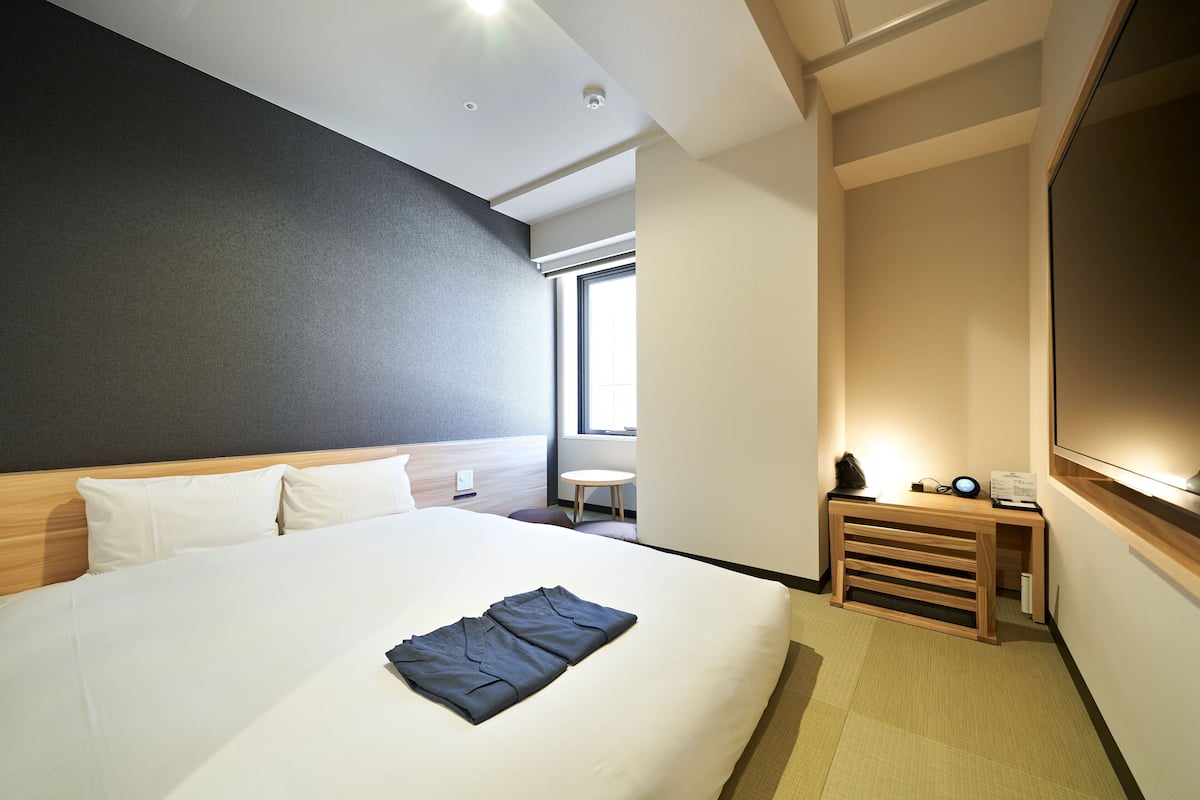 A modern hotel room with a large bed, a small desk, and a television.