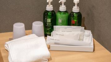 A bathroom with green bottles of body soap, a white towel, and a tray with various personal care items like hair and cotton swabs.
