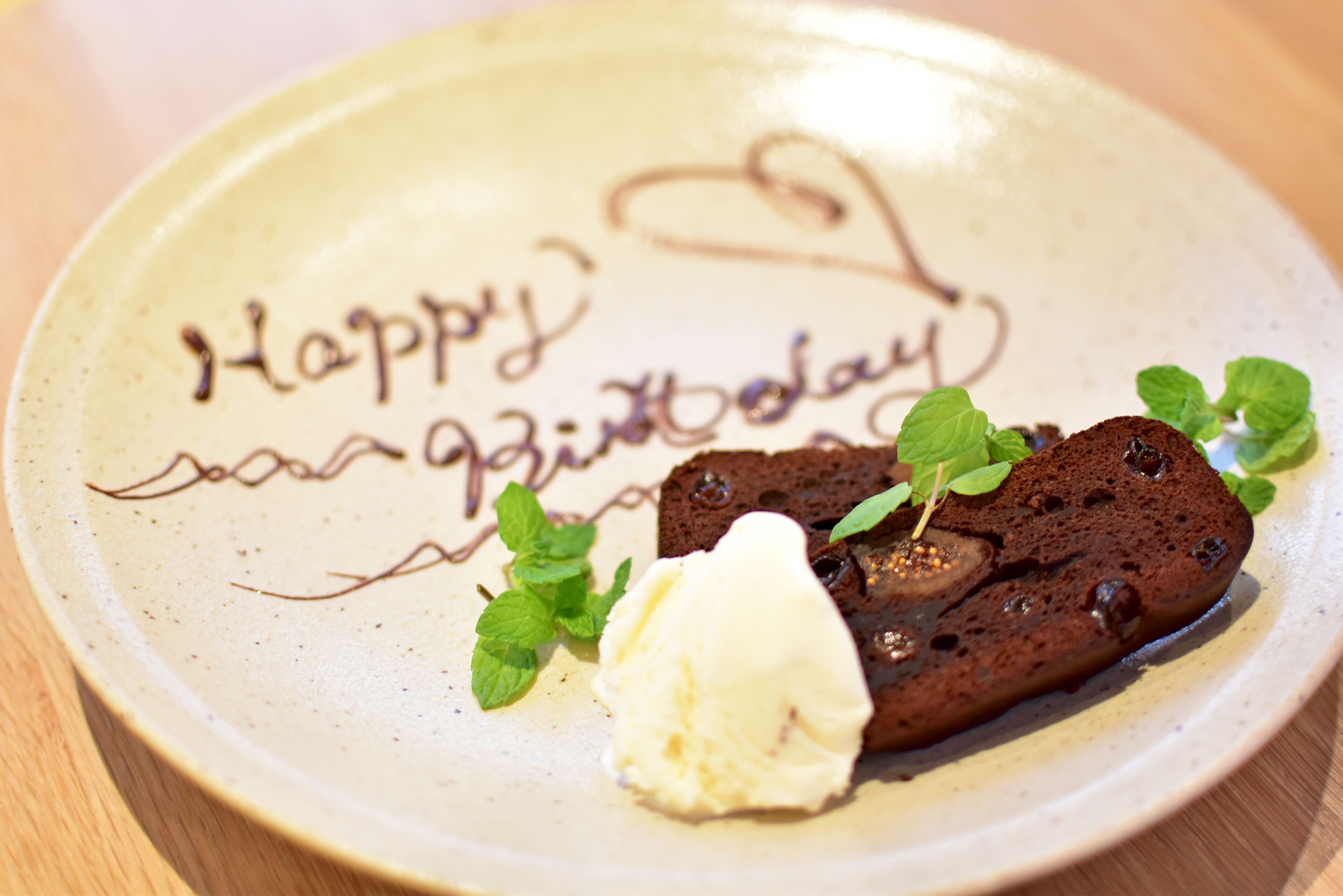 Een bord met chocoladedessert en een bolletje ijs, versierd met een 'Happy Birthday' boodschap.