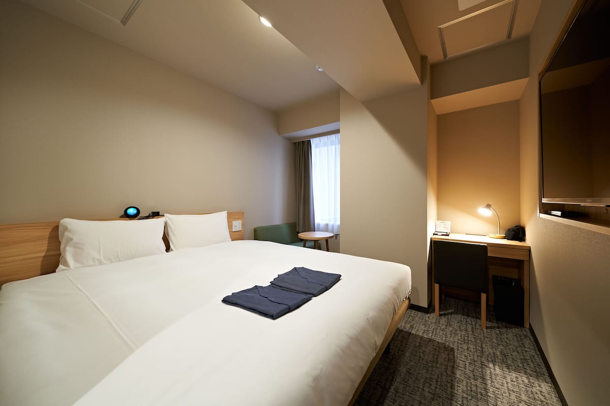 A hotel room with a large bed, a desk, a chair, a small table, and a TV.