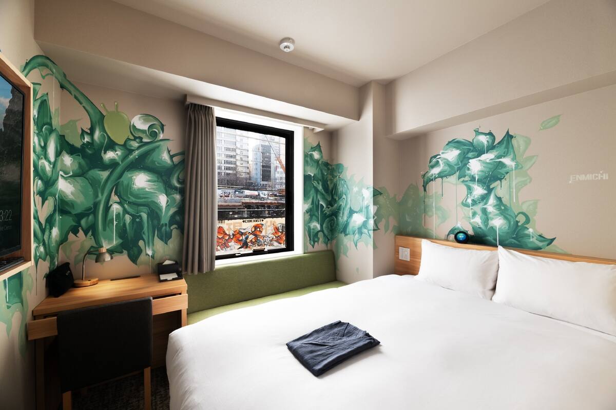 A hotel room with a bed, a desk, and a window with a city view.