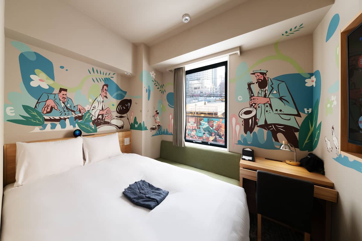 A hotel room with a large bed, a desk, and a window with a city view.