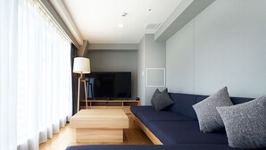 A modern living room with a dark blue sofa, a wooden coffee table, and a large flat-screen TV on a stand. - HOTEL Enmichi (Kawasaki)