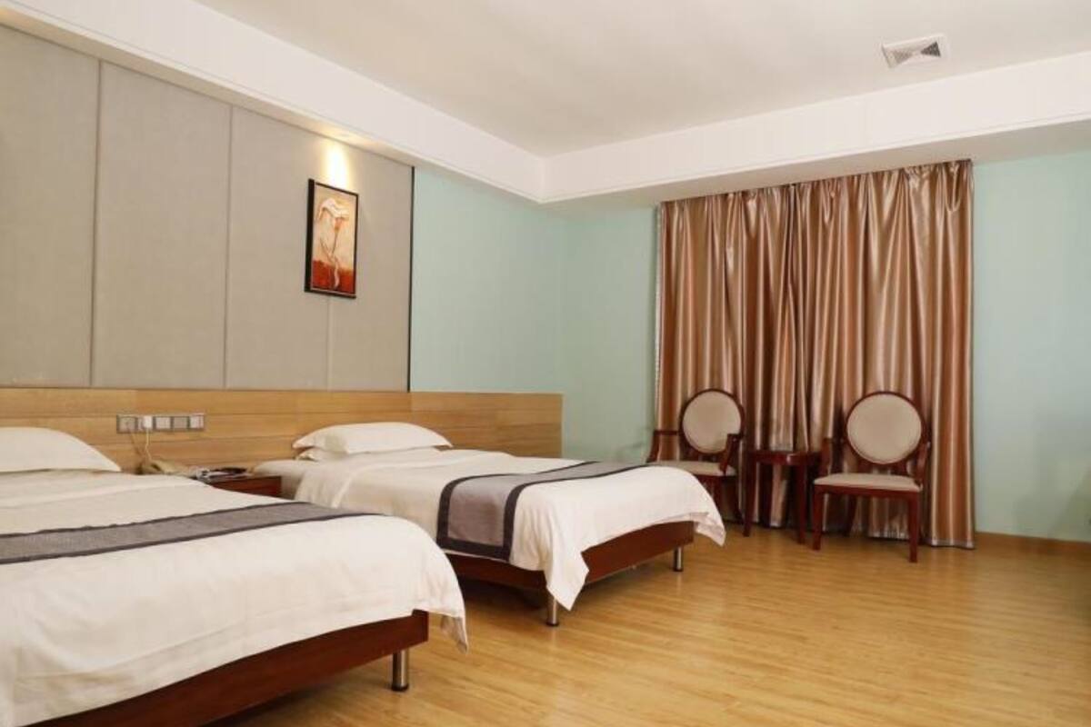 A hotel room with three beds, wooden flooring, a large window with curtains, and a painting on the wall.