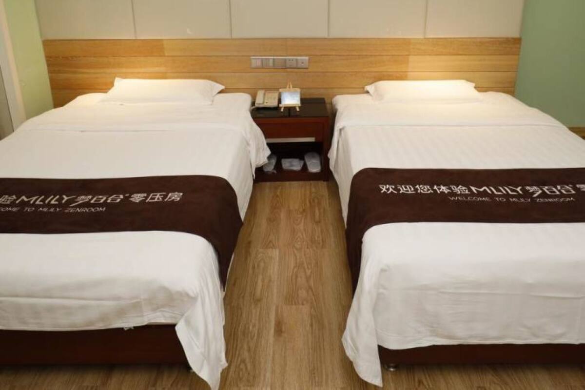 A hotel room with two beds, a wooden headboard, a nightstand, and two framed pictures on the wall.