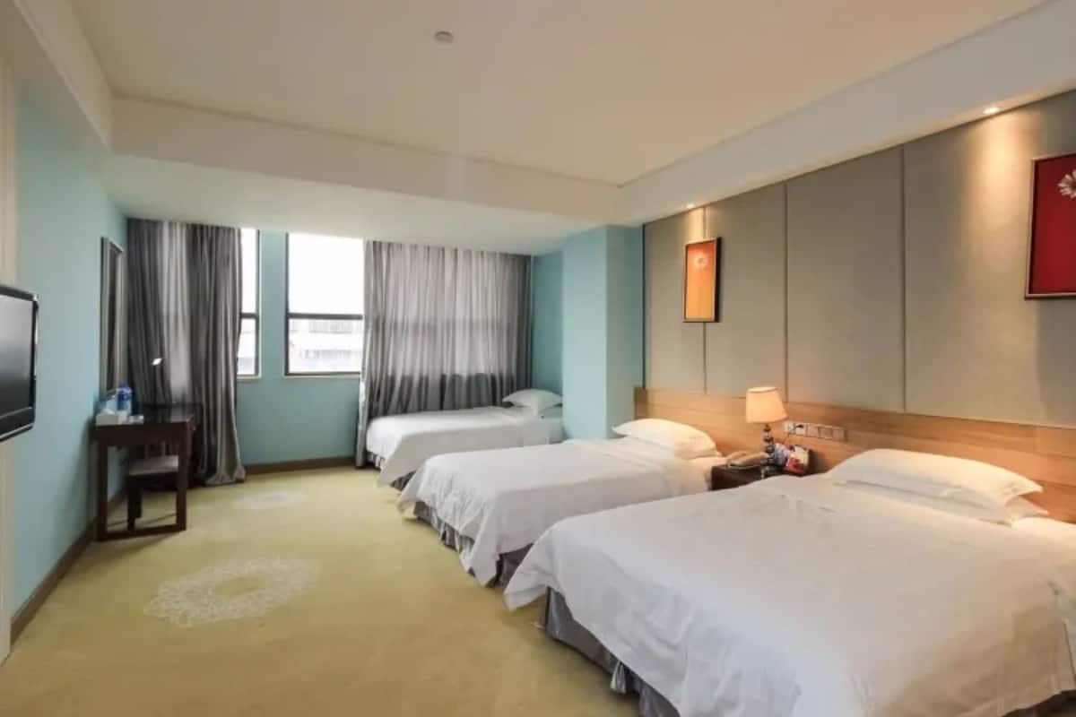 A hotel room with three beds, a television, a desk, and a window with curtains.