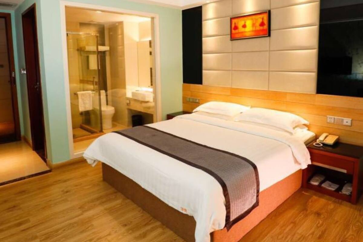 A hotel room with a bed, a bedside table with a phone, and a wall-mounted TV.