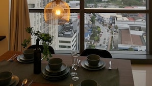 A dining area with a table set for two, a potted plant, and a view of the city through large windows. - Pinnacle PJ by Flexihome (Petaling Jaya)