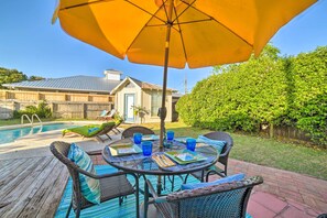 Une terrasse avec une table dressée pour le repas, entourée de chaises en osier, et un parasol offrant de l’ombre.