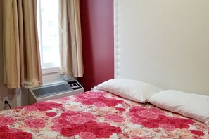 A bedroom with a bed, white pillows, a window with curtains, and an air conditioning unit. - Hotel Kent Chatham (Chatham-Kent)