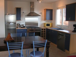 A modern kitchen with a stove, microwave, and refrigerator. There is a dining table with chairs and a window providing natural light. - Villas with private pools in the Cévennes near Ardèche   (SAINT BRES)
