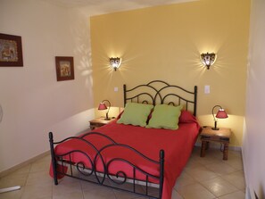 A bed with a red bedspread and green pillows, flanked by two nightstands with lamps, in a room with yellow walls and a tiled floor. - Villas with private pools in the Cévennes near Ardèche   (SAINT BRES)